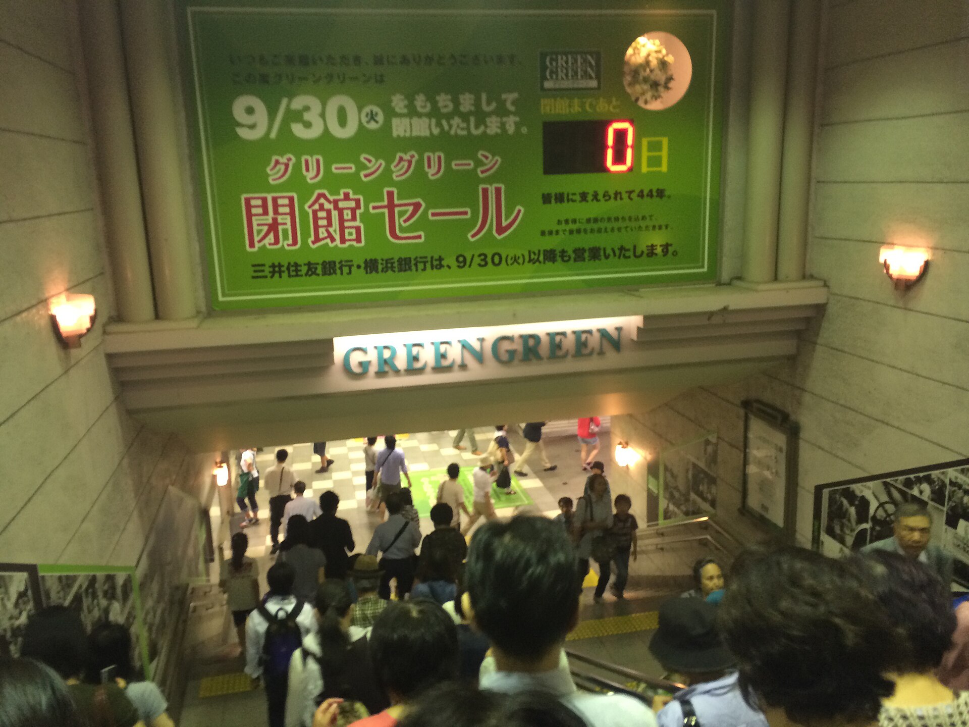 A crowded train station in Japan features a green advertisement for Greengreen sales, reflecting cultural habits.